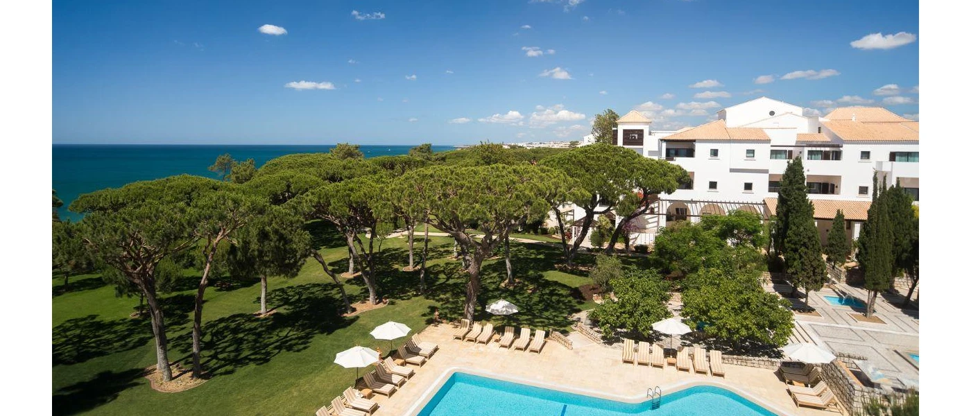 Sunny terrace with multiple pools and trees under a blue sky, with the ocean in the background