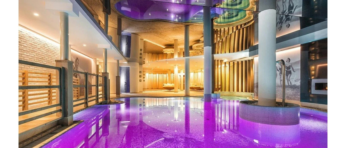 Indoor pool with purple lights, white pillars and black and white retro images of women on the beach