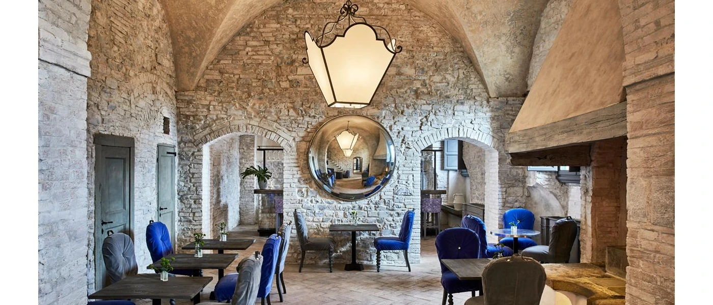Restaurant with cobbled stone walls, blue velvet chairs and a large stone fireplace to the right-hand side