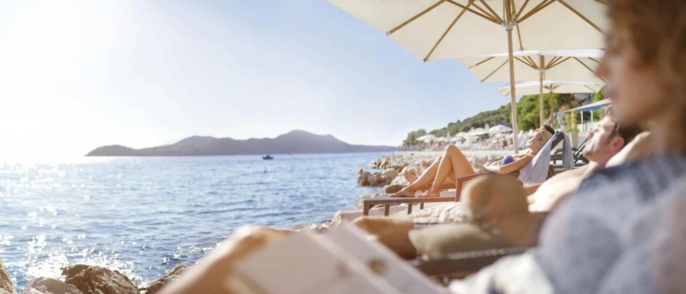 People in swimwear relaxing on loungers under white umbrellas on the seafront