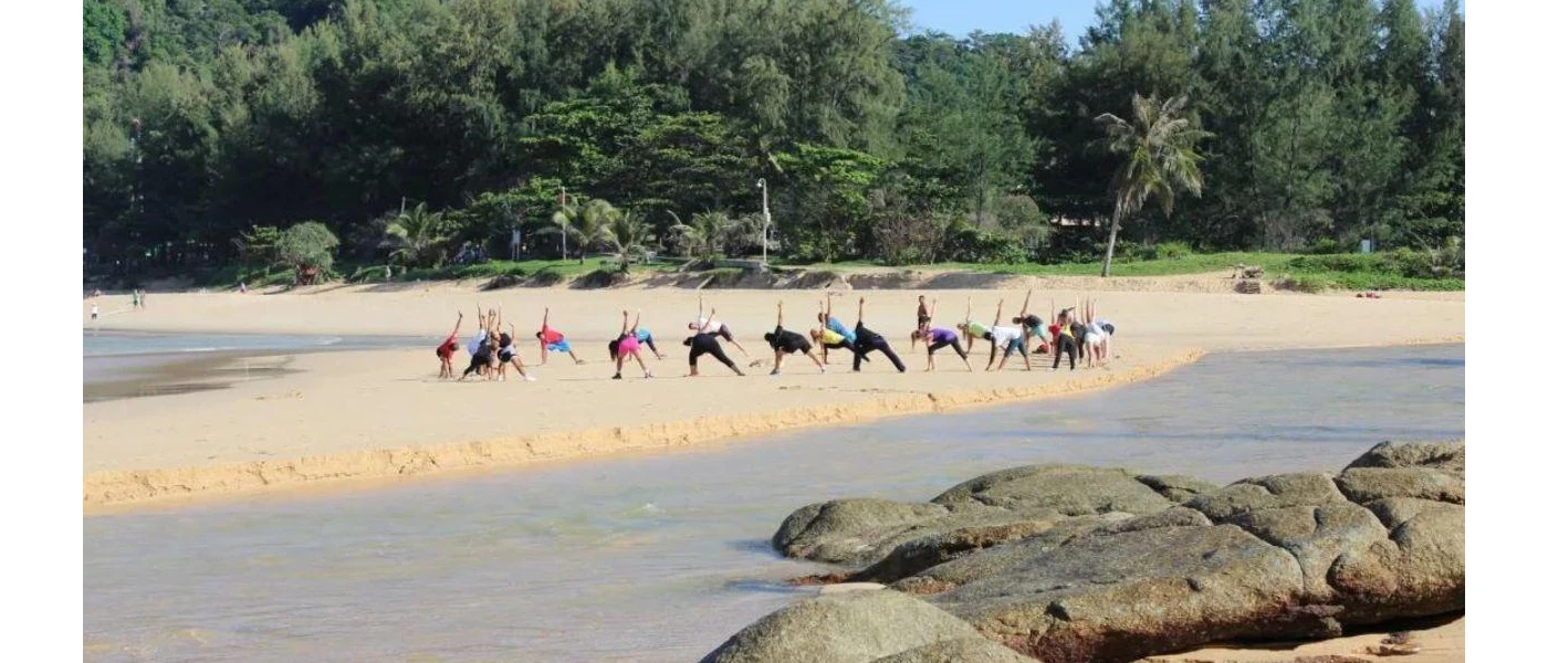 Group practice yoga on a sunny outcrop next to a lake and surrounded by tropical greenery