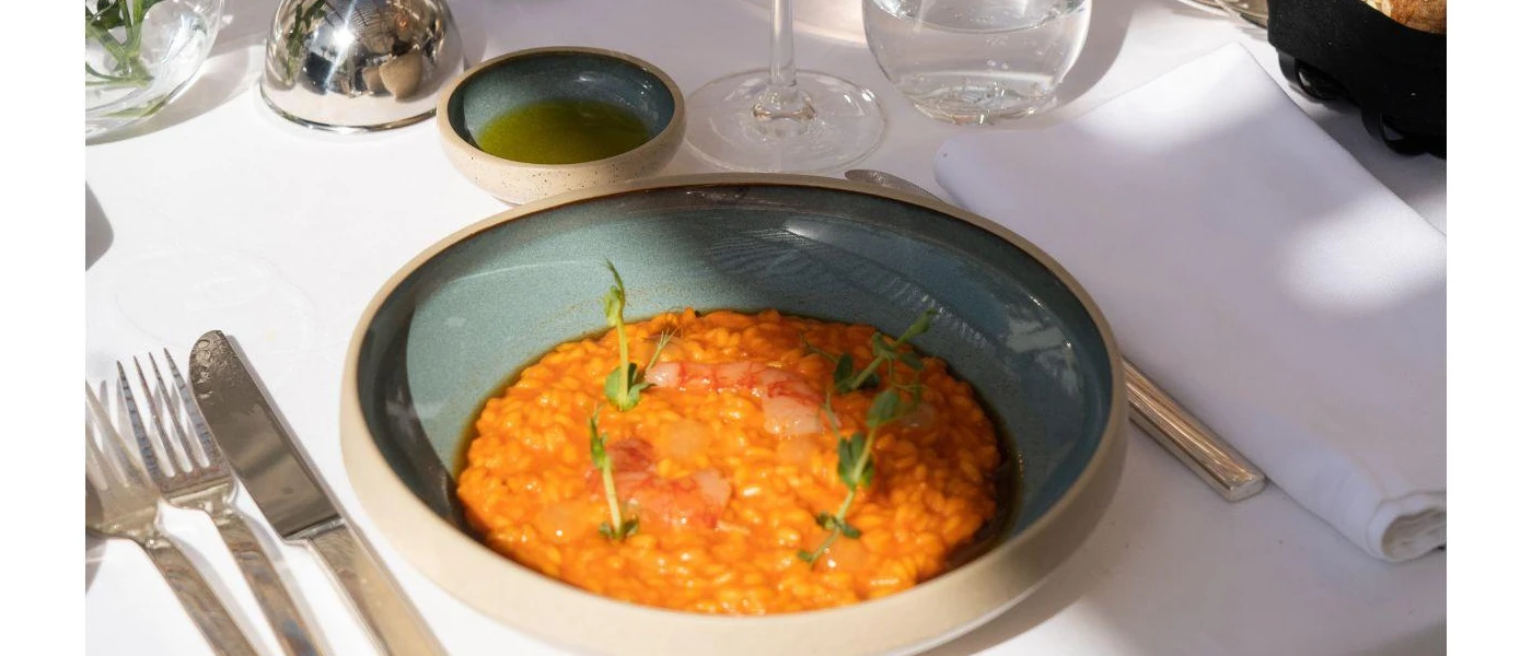 Blue bowl with orange food and a fresh herb garnish inside on a white tablecloth