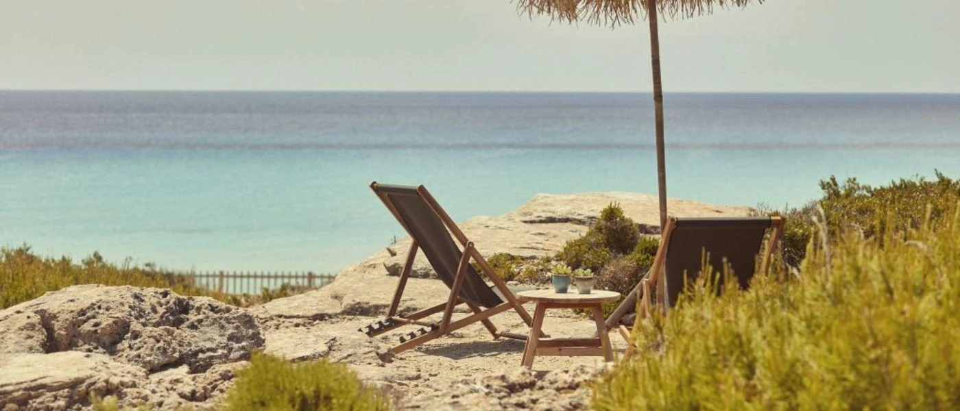 Wooden deck chair and thatched umbrella overlooking the Mediterranean Sea under a blue sky