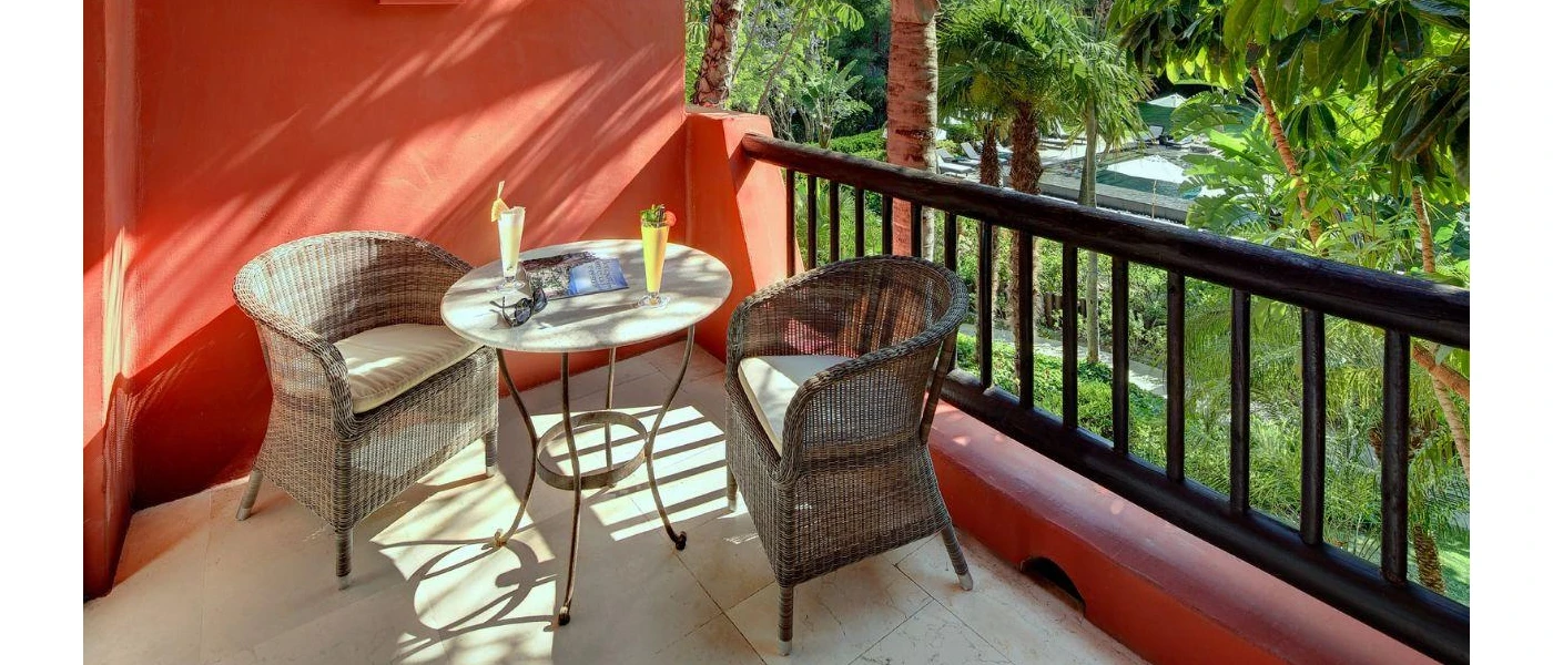 Red-walled balcony with black bannisters and a table and chairs, with cocktails and a pair of sunglasses on the table