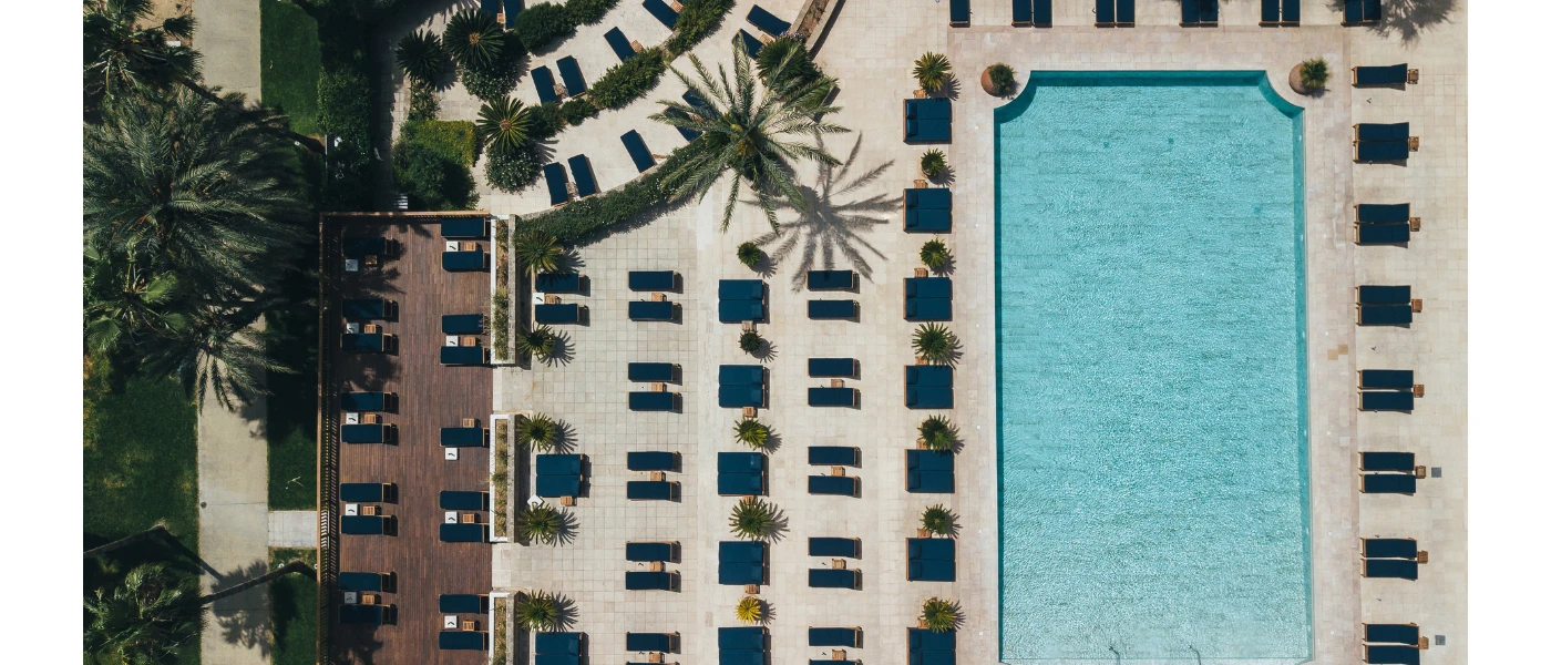 Rectangular pool as seen from above, surrounded by neat rows of daybeds with navy cushions and palm trees