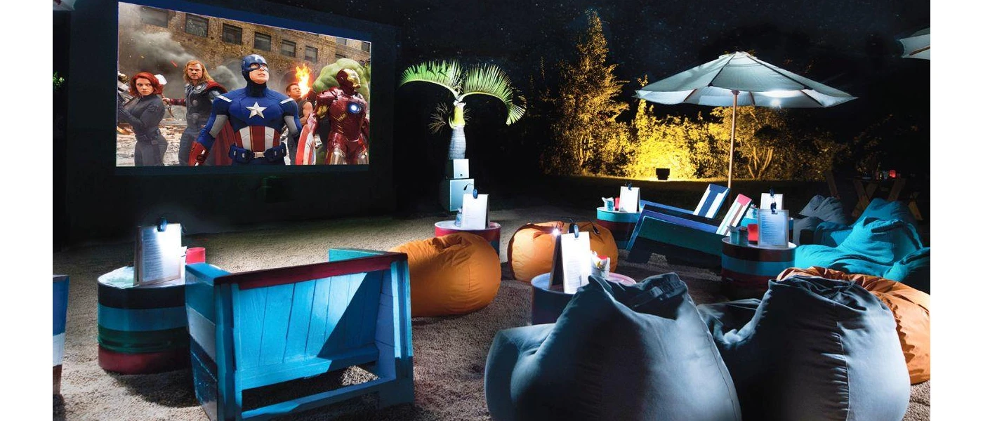 An open-air cinema with bean bags and deck chairs, surrounded by palm trees