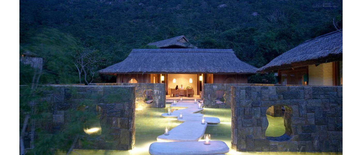 Large white stone slabs making up a pathway leading to a thatched-roof building where two people sit at a desk