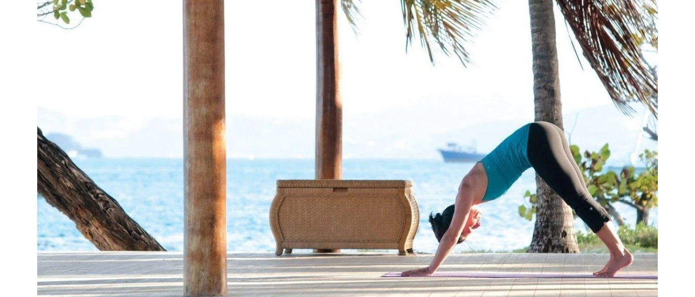 Woman in active wear in downward dog yoga pose practicing by the ocean