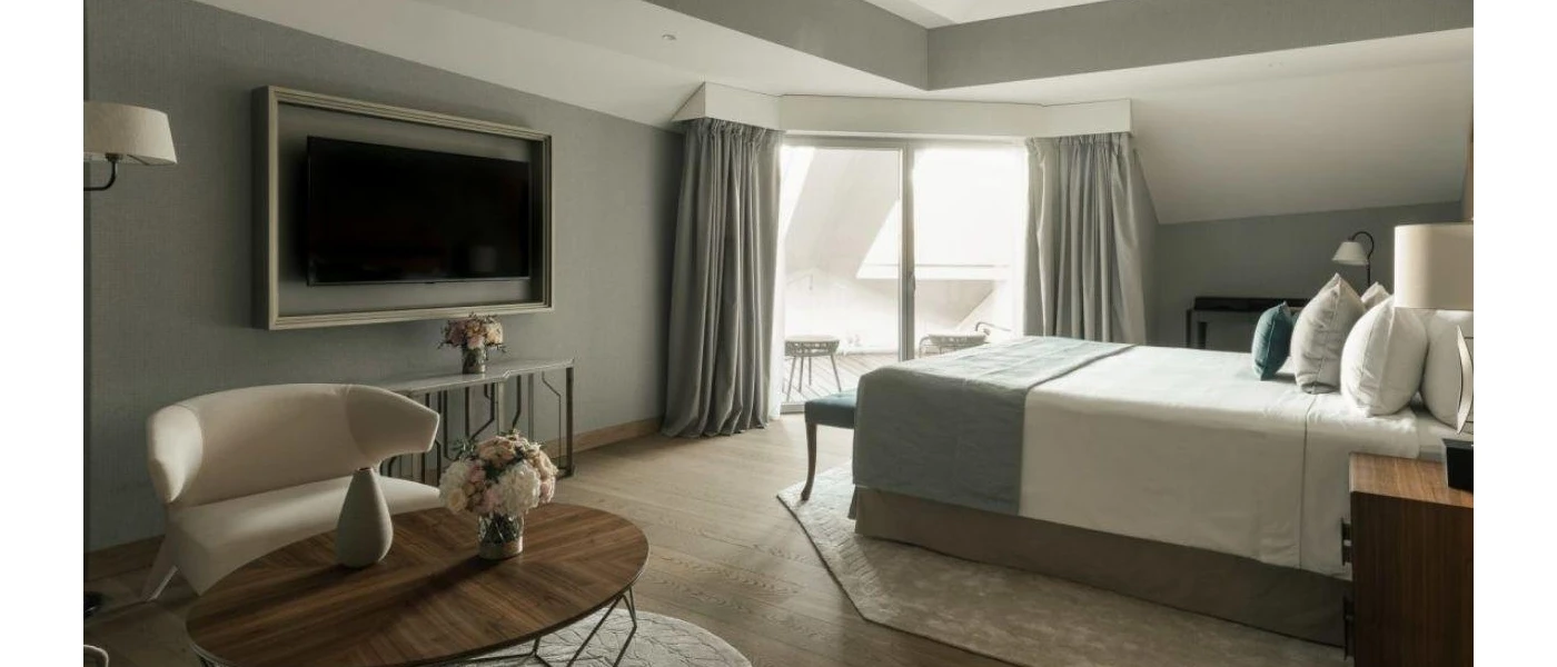 Modern room with grey walls, white bedding, white lamps and armchair and a wall-hung TV