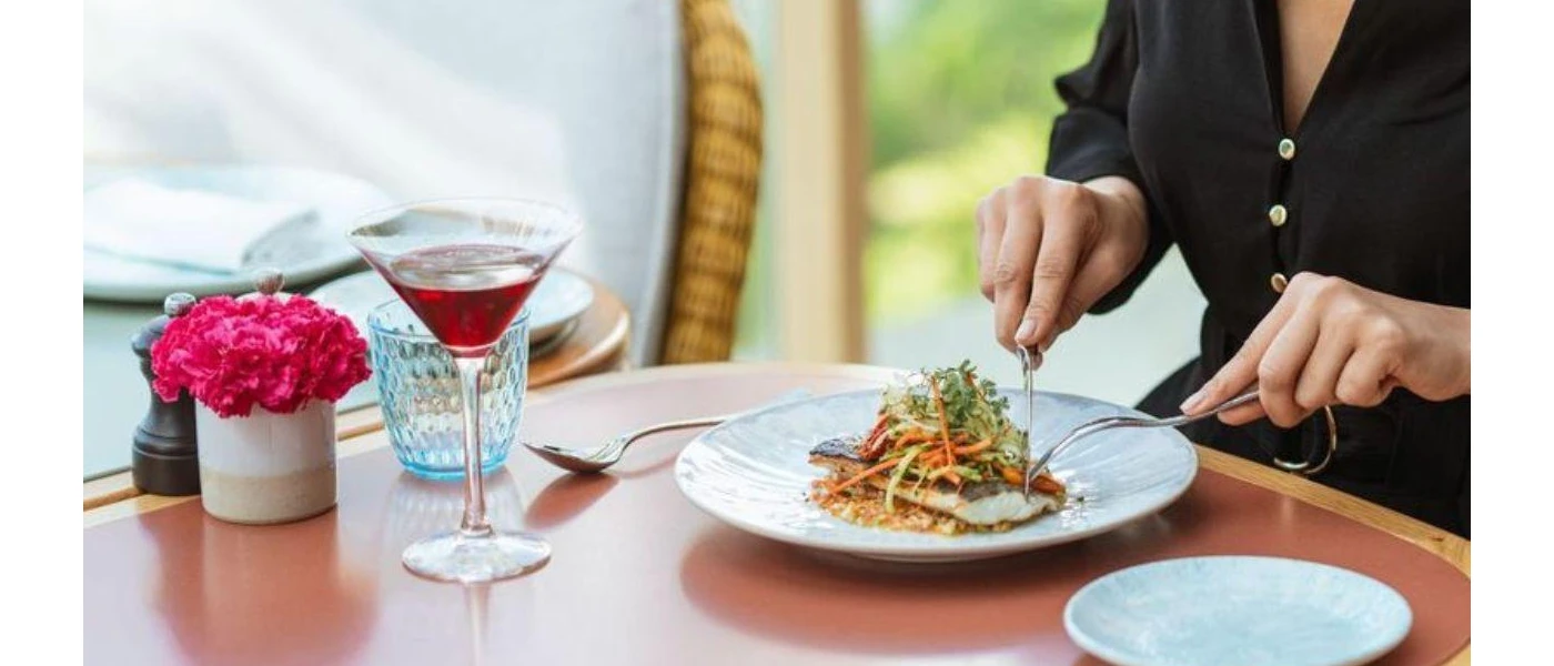 Person in a black shirt cutting into a plate of colourful food with a cocktail in a martini glass beside them