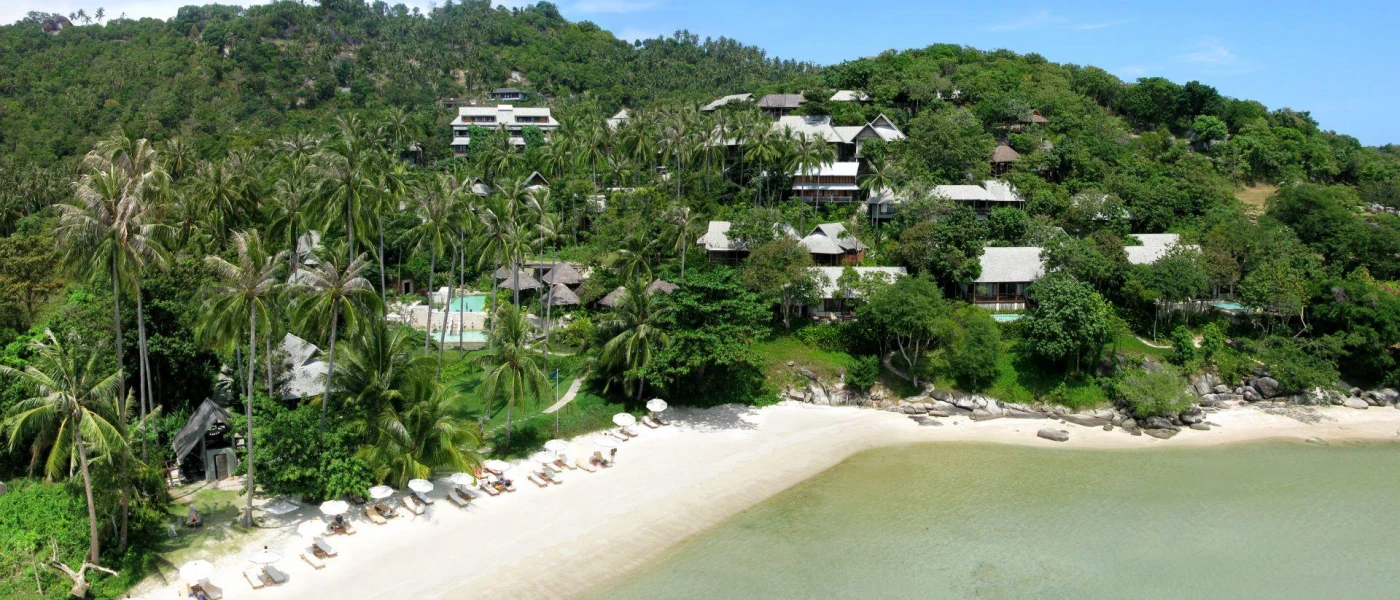 Tropical green hillside with a white-sand beach and pale blue waves under a blue sky