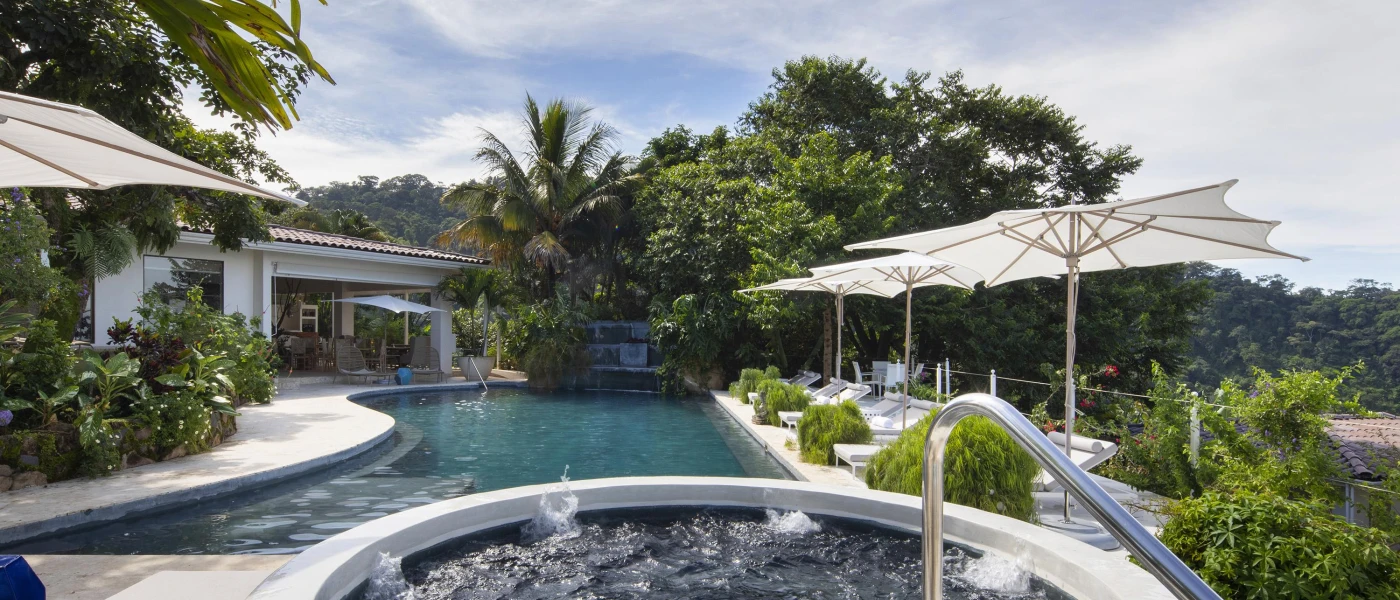 Swimming pool and whirlpool bath surrounded by tropical greenery and parasols