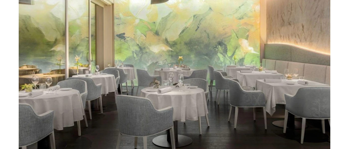 Restaurant with grey chairs and white tablecloths, with a colourful abstract wall mural behind