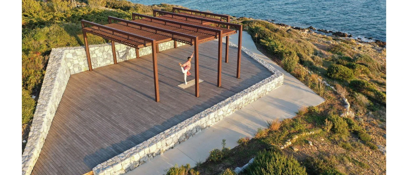 Man on a wooden deck practicing yoga overlooking the ocean and surrounding greenery