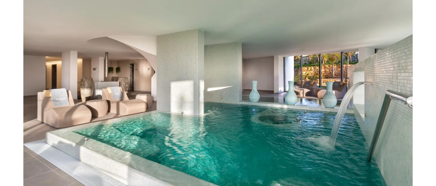 Neutral room with tiled columns, an indoor pool with jets, contemporary cream daybeds and decorative large white pots