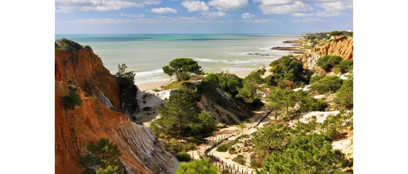 Rugged red-hued cliffs and a leafy path leading down to a sandy beach