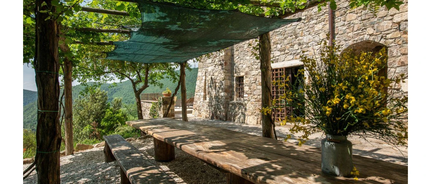 Covered stone terrace with tables and a vase with flowers, overlooking green hills