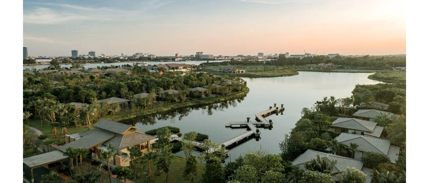 Grey-roofed resort cloaked in greenery on a riverside, with a wooden jetty jutting out into the water