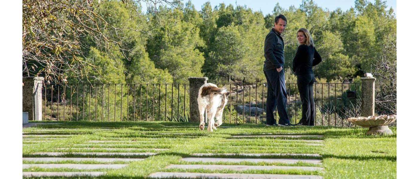 Couple in black look back at their dog in a lush garden