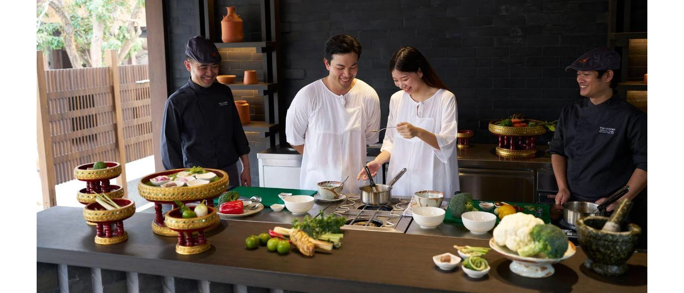 Two guests in white experiment at a cooking station as two chefs look on