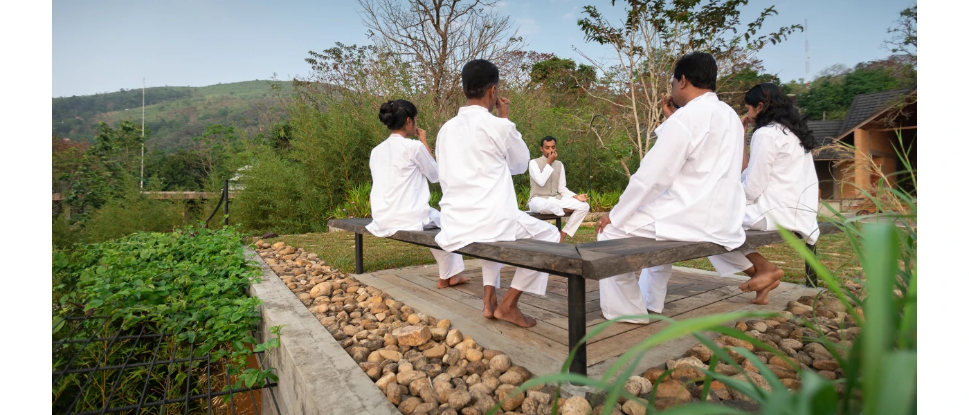 Group in white sits on a bench in an outdoor courtyard overlooking green hills