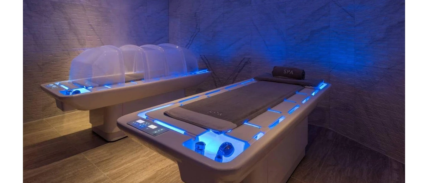 Two futuristic looking treatment beds with blue lighting in a dark spa cabin