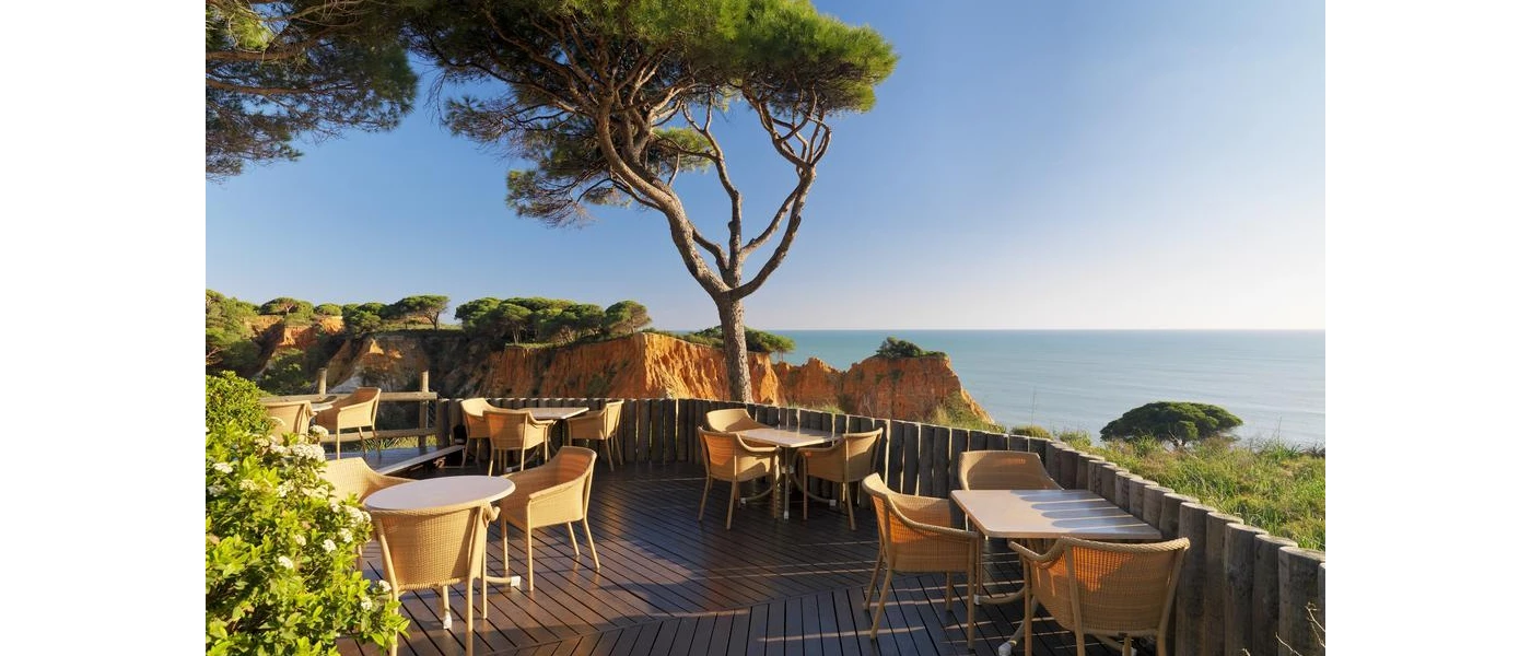 Al fresco terrace with wooden tables and chairs and a view of the surrounding cliffs, greenery and ocean