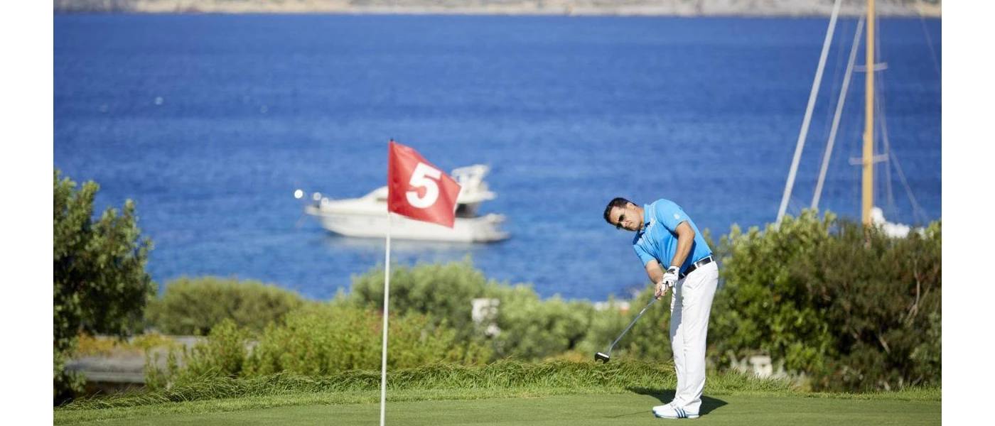 Man swings a golf club on greens in front of the sea