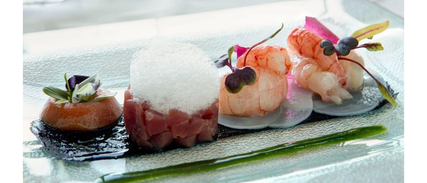 Miniature seafood bites on a plate with a green jus, one topped with foam