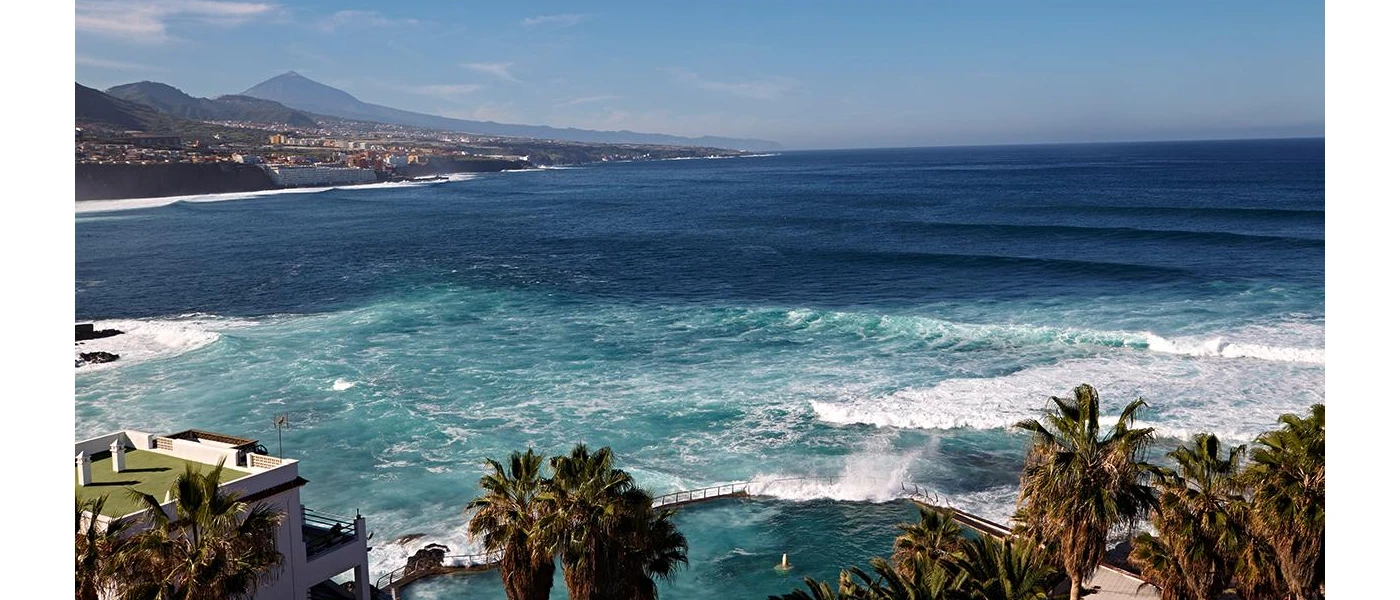 Palm trees, seawater pool and the Atlantic Ocean with mountains in the foreground