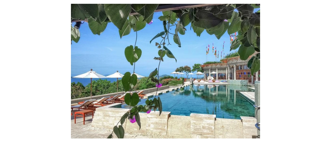 Stone-walled swimming pool surrounded by white parasols and overlooking the sea