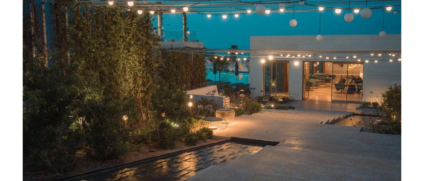 Stone steps down to a hotel lobby entrance, fringed by greenery and fairy lights under a night sky