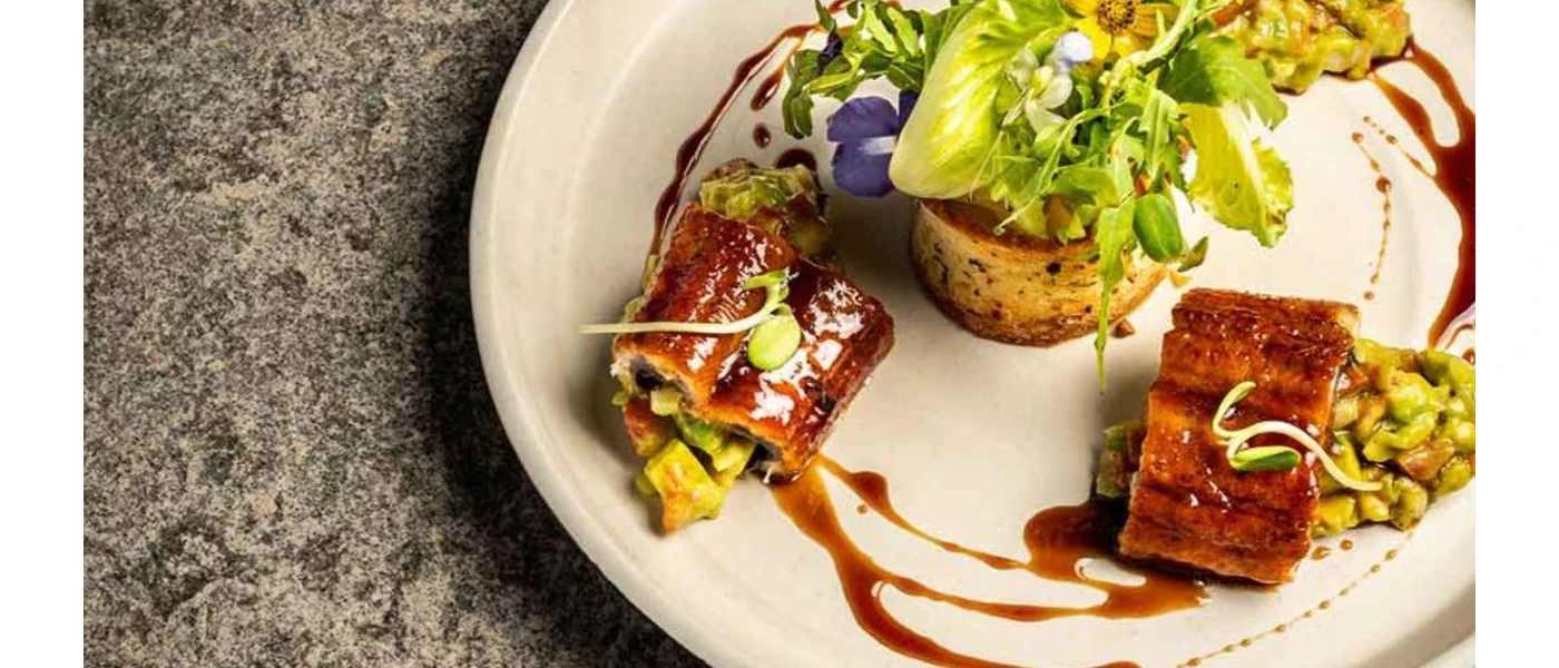 Plate of gourmet food stacked with a salad garnish, vegetables and edible flowers and drizzled in a brown sauce