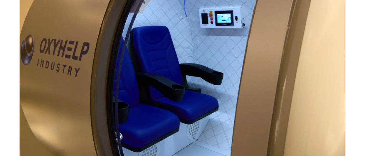 Door open on an oxygen chamber with two blue chairs and a side panel