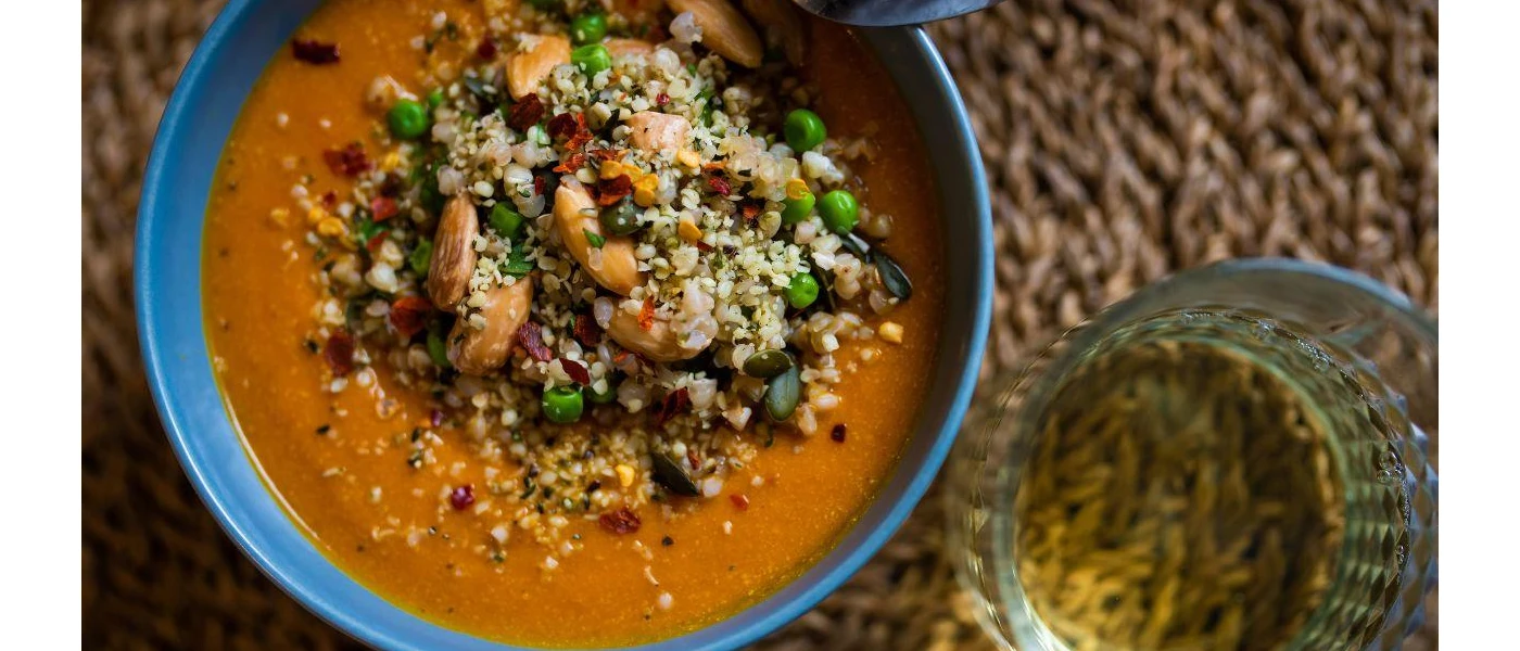 Blue bowl of a carrot-like soup topped with grains and vegetables