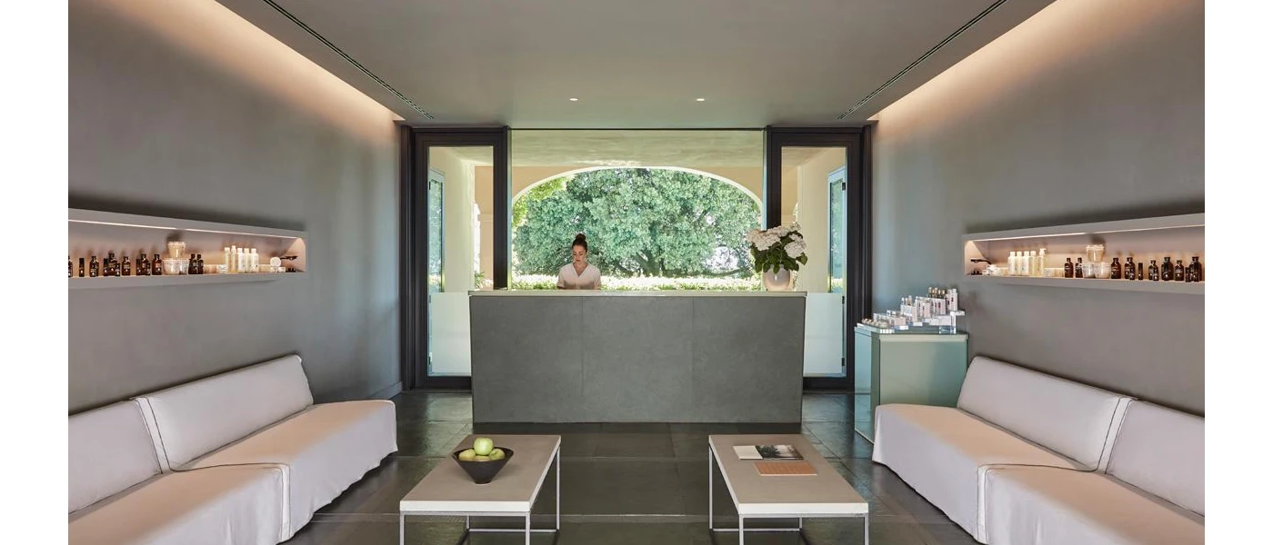Grey reception area with shelves of bottles on the wall and a woman in uniform