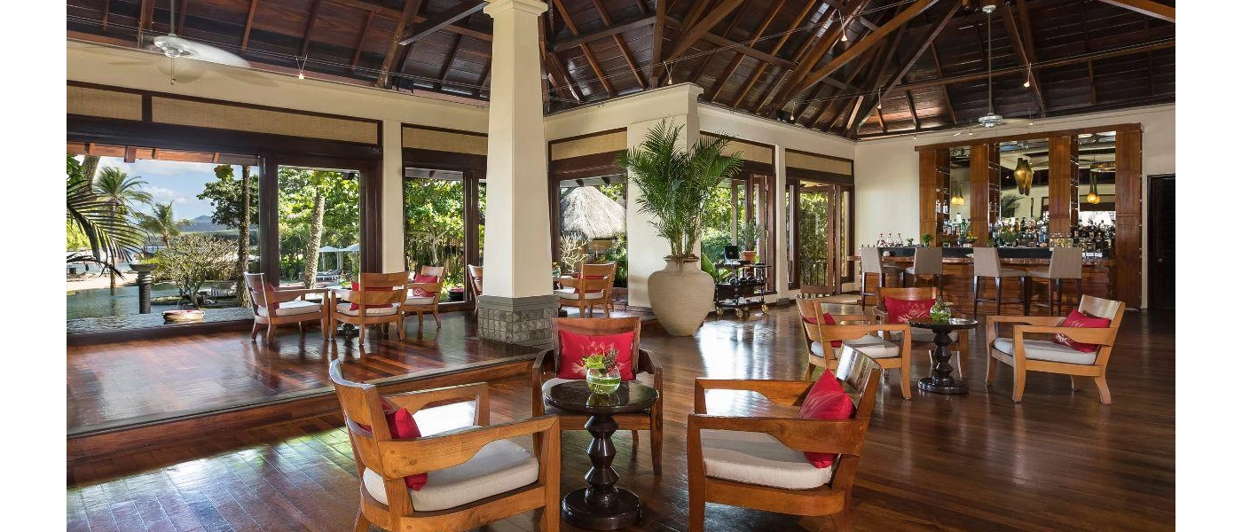 Rustic interior with wooden ceiling beams and floors, wooden chairs and floor-to-ceiling windows looking out to tropical greenery