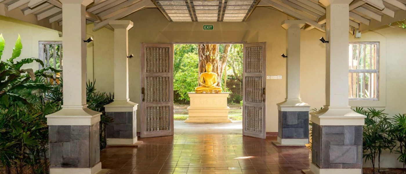 Entranceway with terracotta floor tiles, white pillars, potted plants and a gold Buddha statue