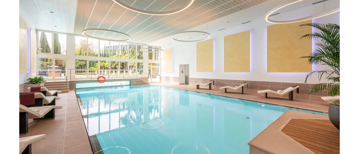 Large indoor swimming pool with floor to ceiling windows overlooking hotel's gardens. 