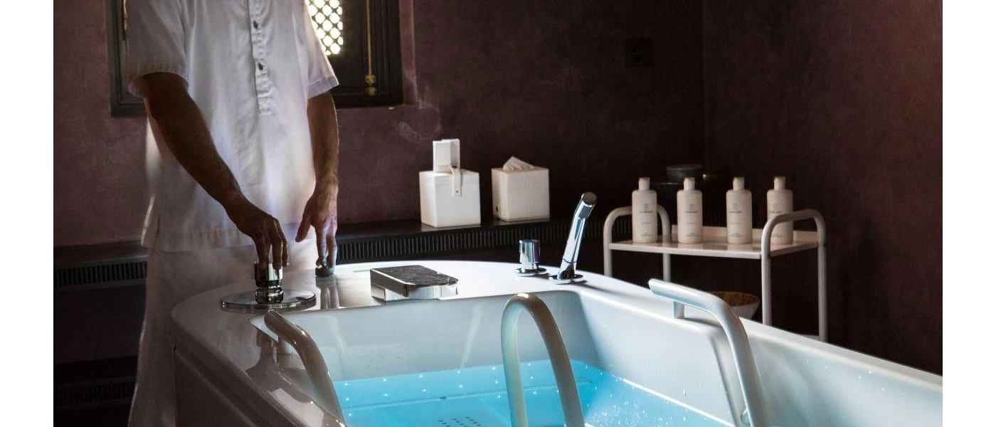 Person in white running a bath with oils and lotions in the background