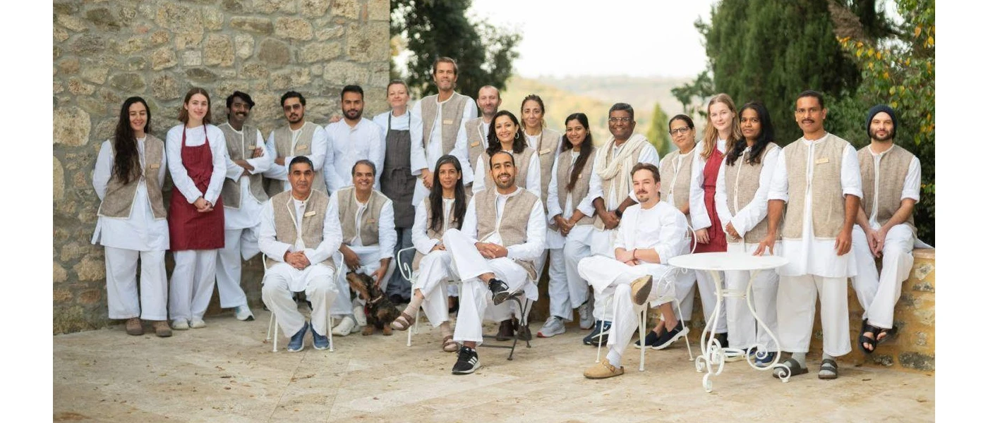Group of people in loose fitting white clothes and waistcoats with name badges smile for a picture 