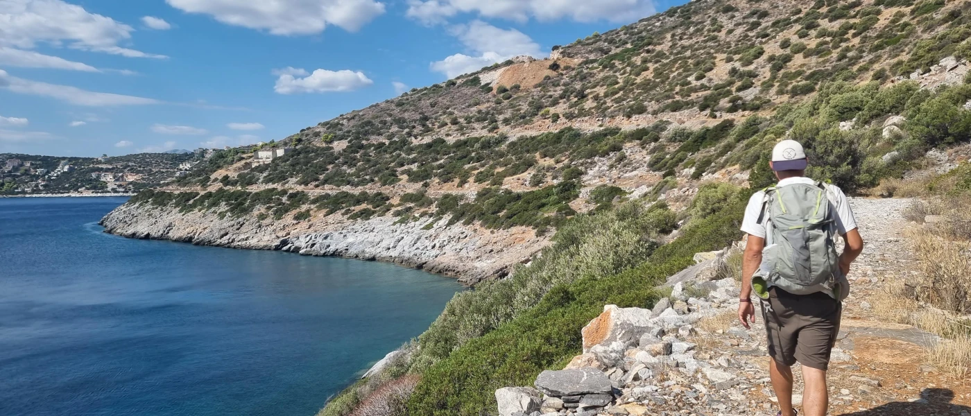 Man in shorts, a baseball cap, trainers and a rucksack walks along the rugged coastline