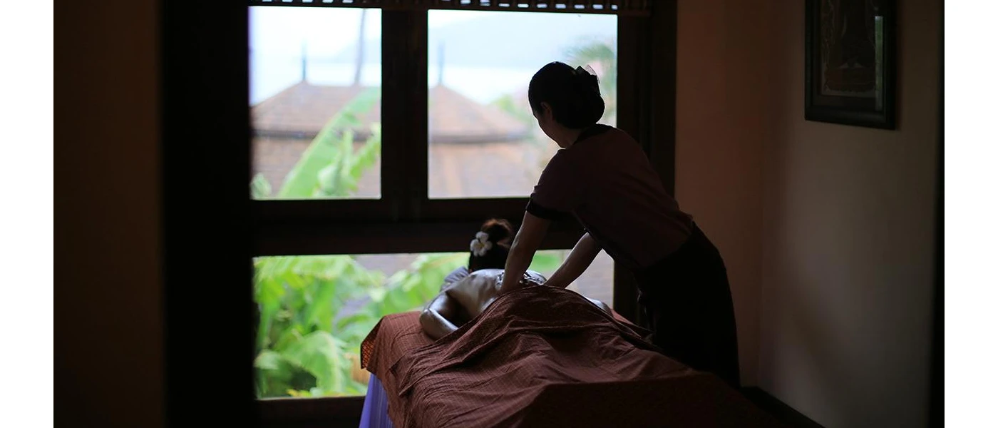 Woman lies on her front with a flower in her hair in a darkened room, as a therapist massages her back