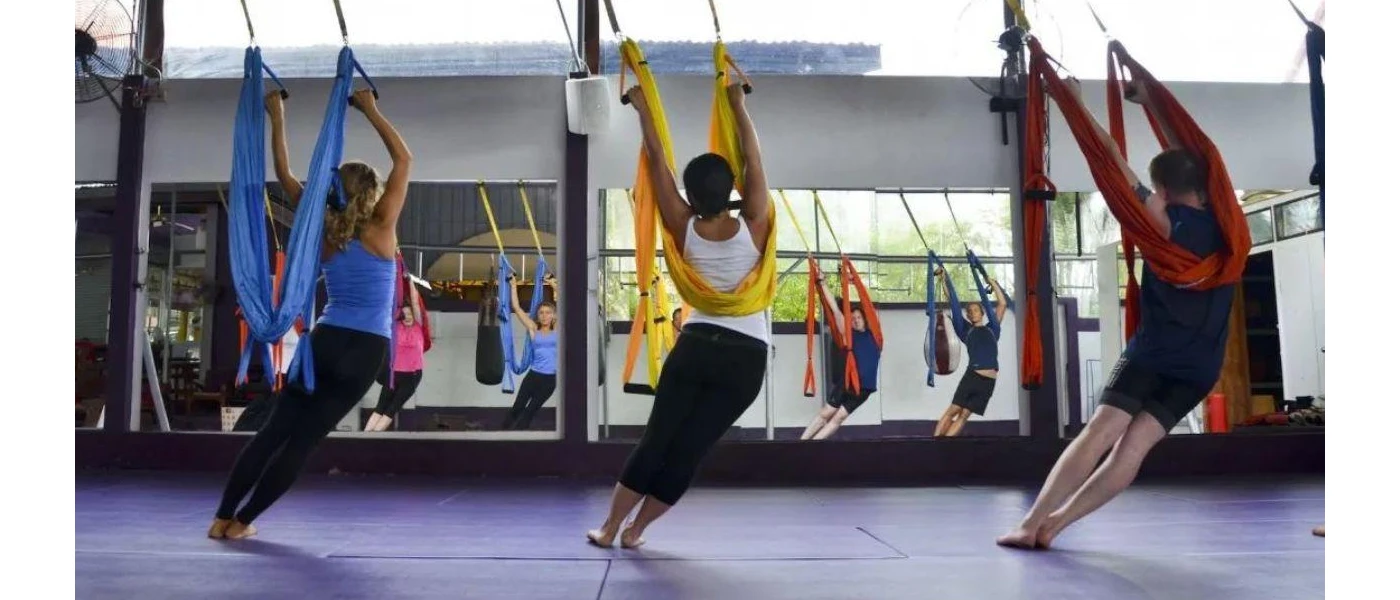 Group in active wear hang from ribbon harnesses opposite a mirror in a fitness class