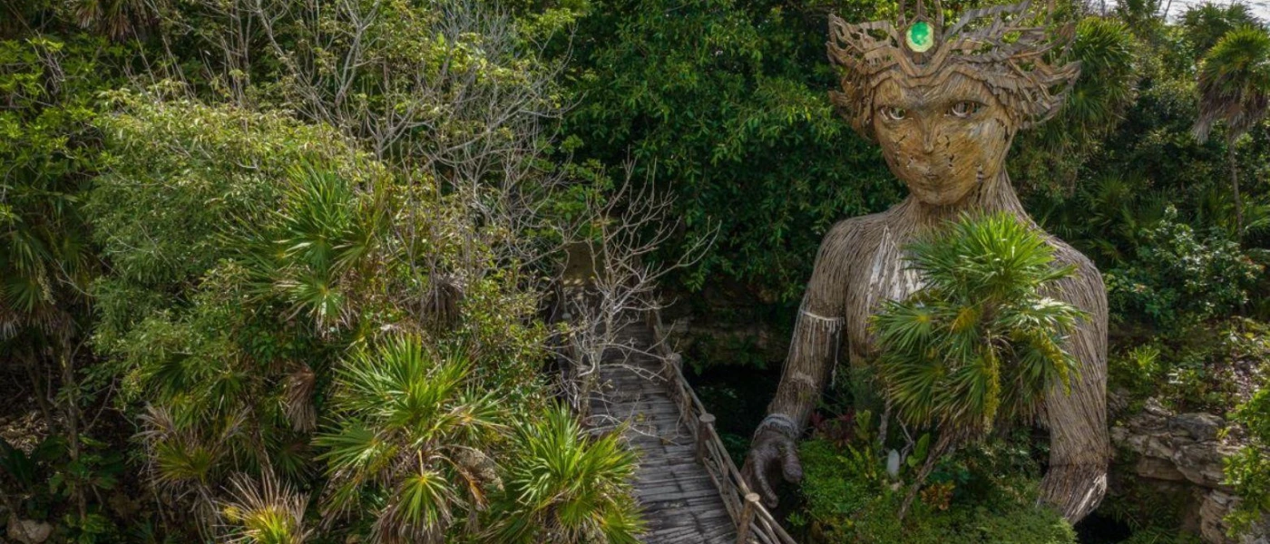Giant wood-carved sculpture among mangroves, depicting a woman with a crown and holding greenery in her arms