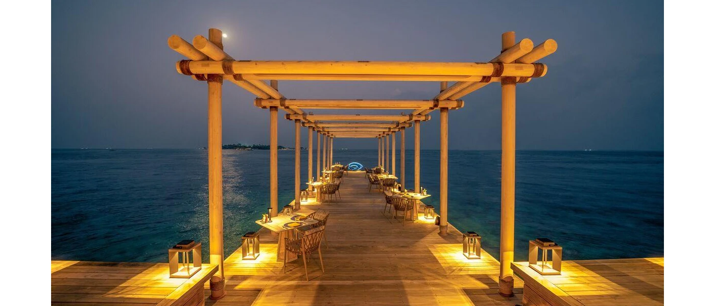 Wooden lantern-lit jetty laid out with tables and chairs as the sky darkens