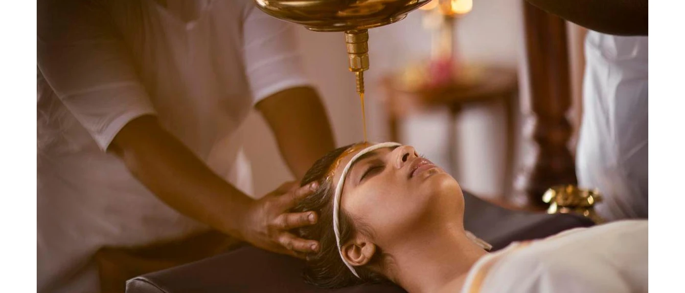 Woman lies on her back with her eyes closed as oil drips onto her scalp and a therapist holds her head