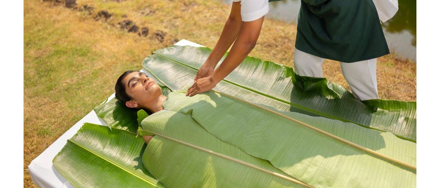 Female having an outdoor treatment done where therapist is wrapping her in banana leaves 