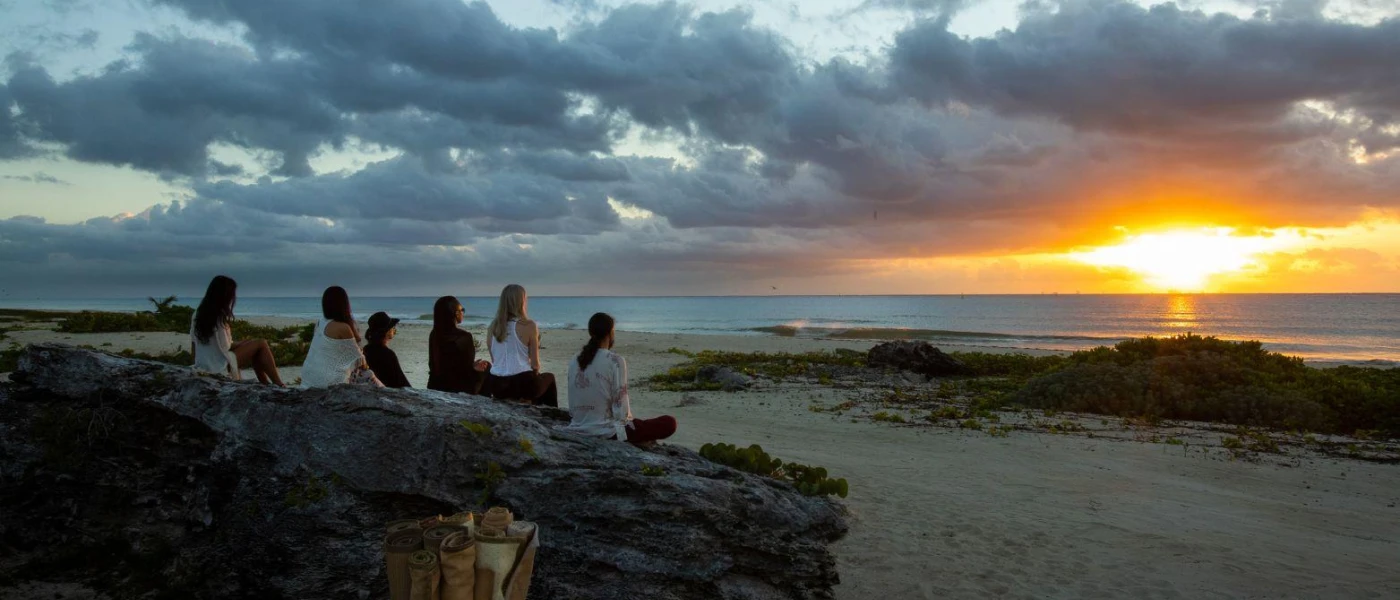 Group sitting on rocks on the beachfront, watching the sun rise or set above the ocean