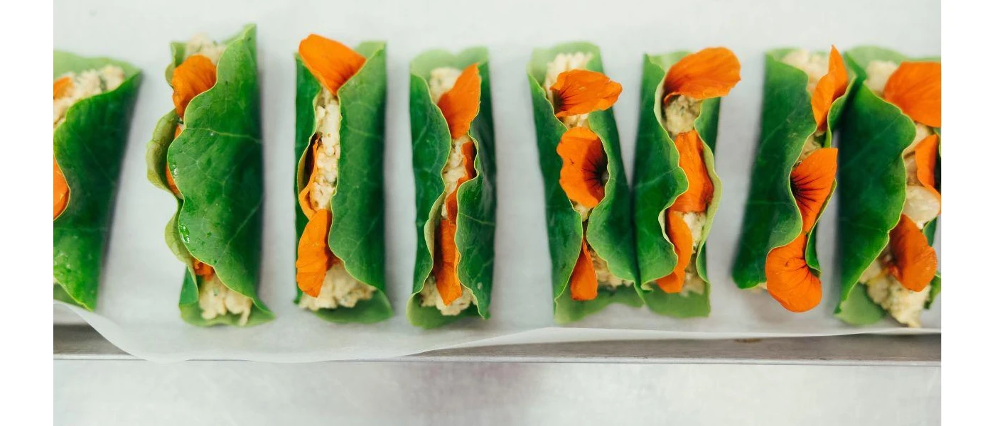 A plate of green leaves rolled up and stuffed with rice and orange edible flowers